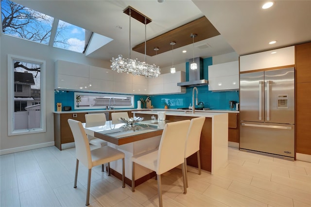 kitchen with tasteful backsplash, stainless steel fridge with ice dispenser, modern cabinets, light countertops, and wall chimney range hood