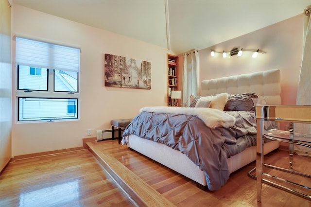 bedroom with vaulted ceiling, baseboard heating, and wood finished floors