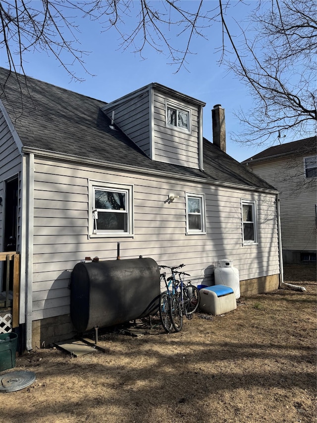 back of house with a shingled roof, a chimney, and heating fuel