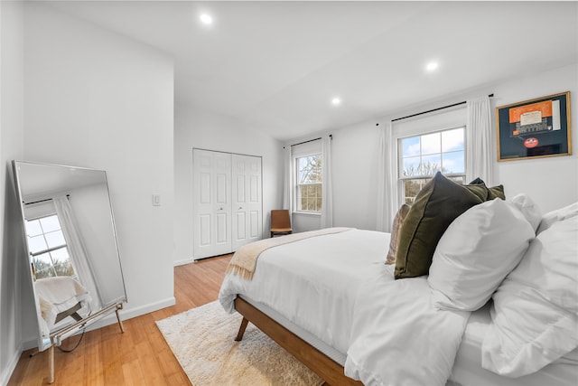 bedroom with light wood-type flooring, lofted ceiling, recessed lighting, a closet, and baseboards