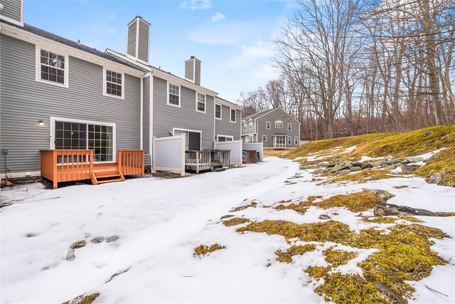 snow covered rear of property with a deck and a chimney