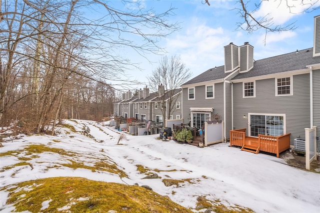 snow covered house with a shingled roof, a wooden deck, a residential view, and a chimney