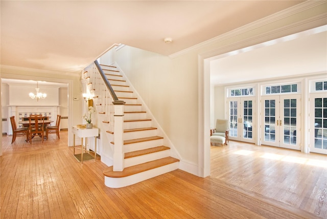 stairway with hardwood / wood-style flooring, a notable chandelier, baseboards, french doors, and crown molding