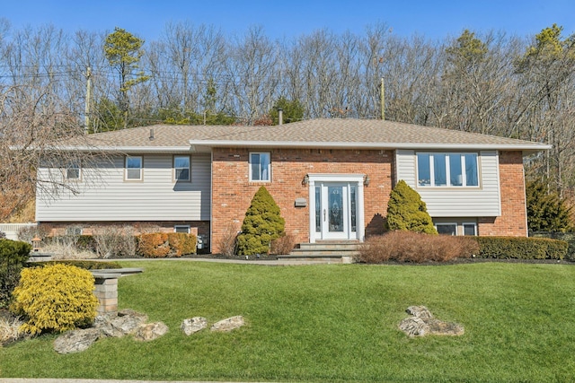 bi-level home with roof with shingles, a front lawn, and brick siding