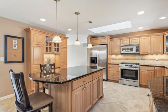 kitchen with a skylight, hanging light fixtures, backsplash, appliances with stainless steel finishes, and a kitchen bar