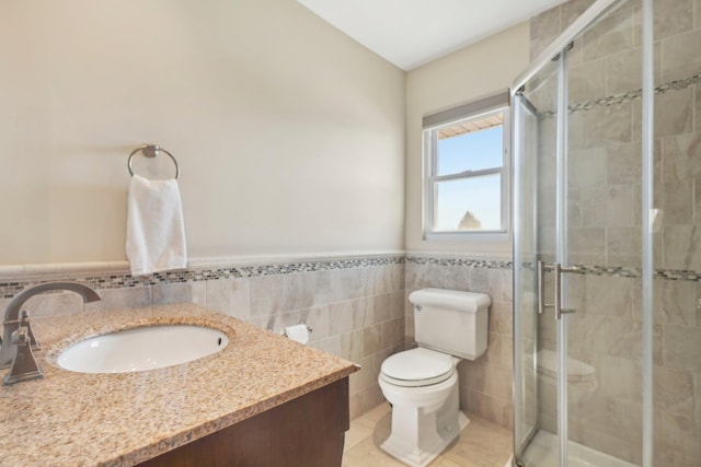 bathroom featuring toilet, vanity, tile walls, wainscoting, and a stall shower