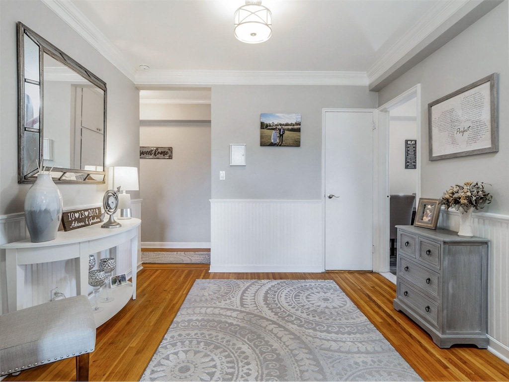 interior space with a wainscoted wall, wood finished floors, and crown molding
