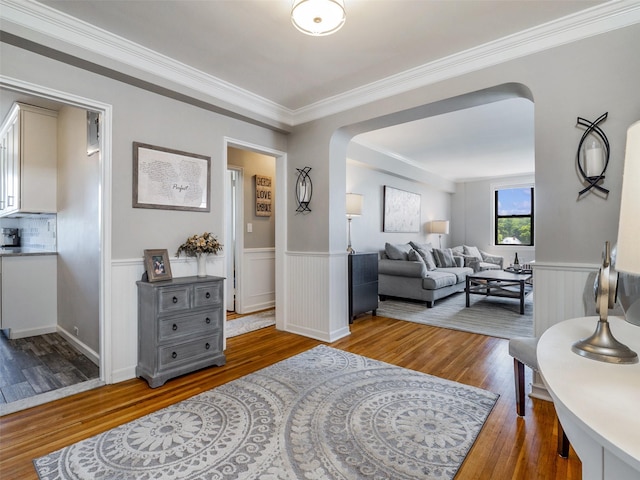 living area featuring arched walkways, crown molding, wainscoting, and hardwood / wood-style flooring