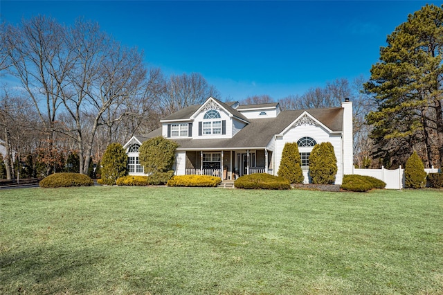 view of front of home with a porch, a front lawn, a chimney, and fence