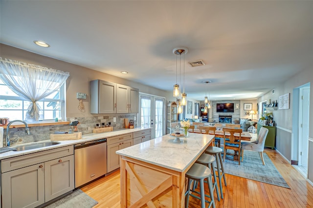 kitchen featuring gray cabinetry, a sink, open floor plan, stainless steel dishwasher, and a center island