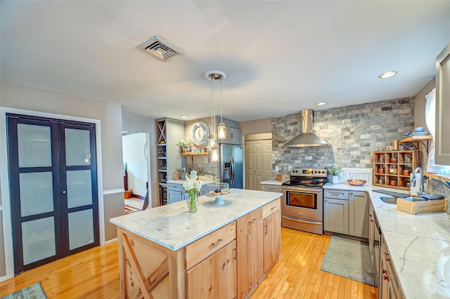 kitchen with a center island, visible vents, light brown cabinetry, appliances with stainless steel finishes, and wall chimney range hood