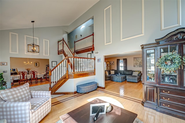 living room featuring an inviting chandelier, light wood-style flooring, stairs, and high vaulted ceiling