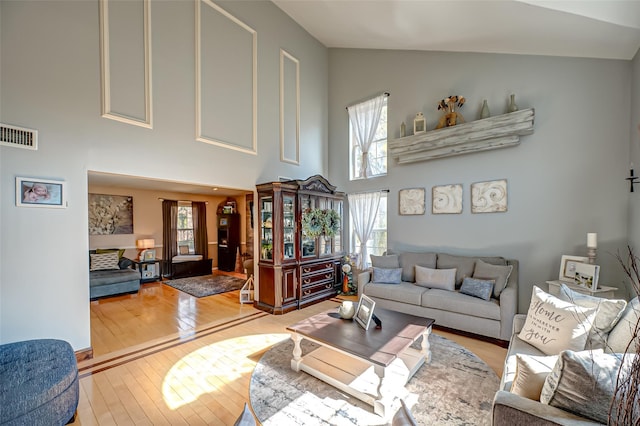 living area with high vaulted ceiling, wood finished floors, and visible vents