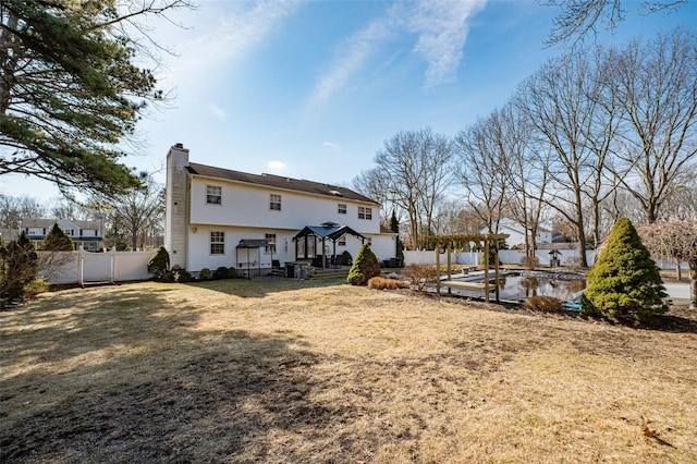 rear view of house featuring a chimney, fence, and a yard