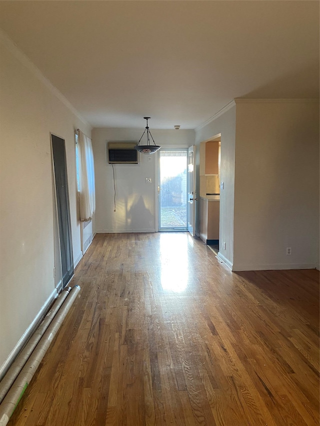 unfurnished living room with ornamental molding, a wall mounted air conditioner, baseboards, and wood finished floors