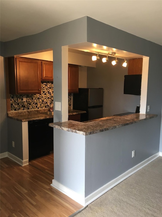 kitchen featuring black dishwasher, decorative backsplash, brown cabinets, freestanding refrigerator, and a peninsula