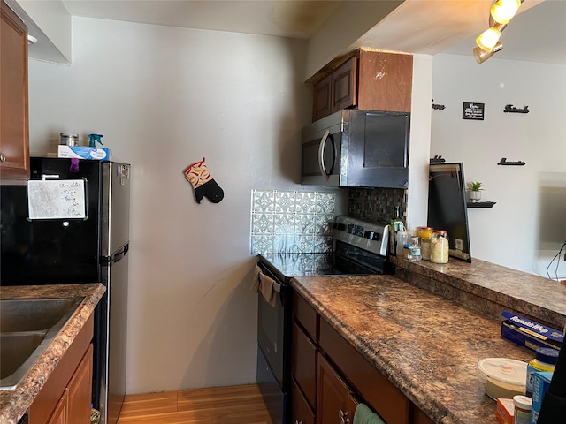 kitchen with dark countertops, light wood-style flooring, decorative backsplash, appliances with stainless steel finishes, and brown cabinetry