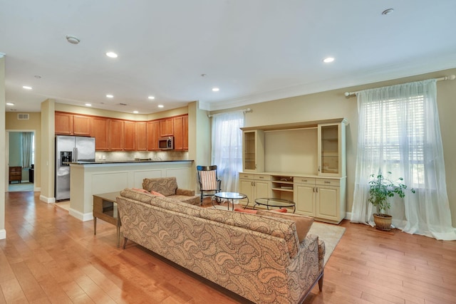 living area with light wood finished floors, recessed lighting, visible vents, ornamental molding, and baseboards