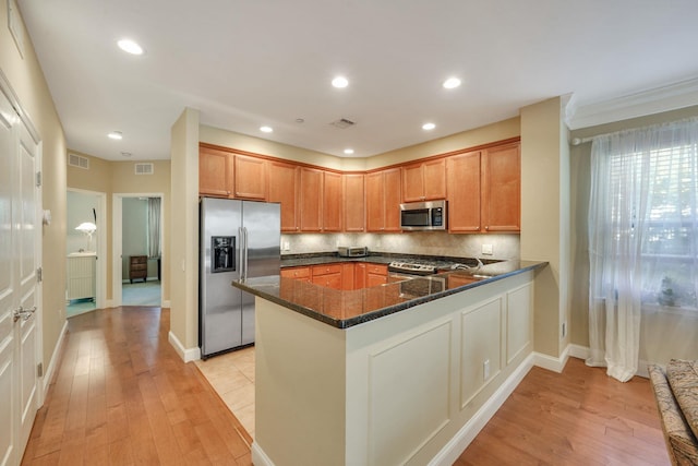 kitchen with backsplash, light wood-style flooring, appliances with stainless steel finishes, dark stone counters, and a peninsula