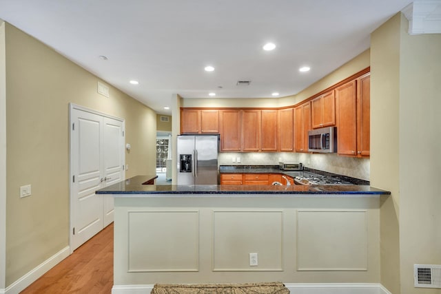 kitchen with visible vents, dark stone counters, brown cabinets, a peninsula, and stainless steel appliances