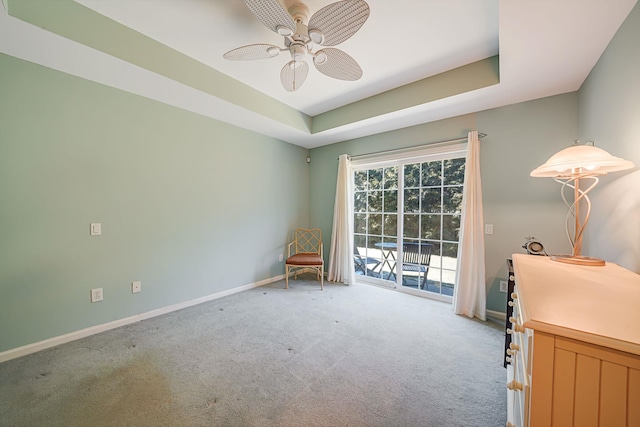 living area featuring carpet floors, baseboards, a tray ceiling, and a ceiling fan