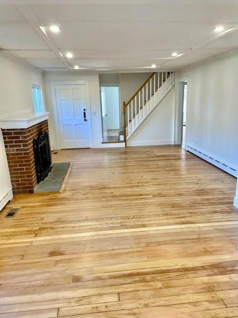 unfurnished living room featuring light wood-style flooring, recessed lighting, a fireplace, stairway, and baseboard heating