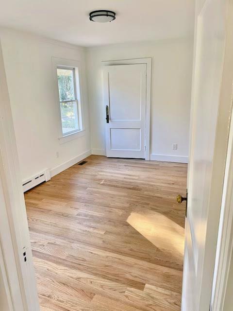 unfurnished room featuring a baseboard radiator, light wood-style flooring, visible vents, and baseboards