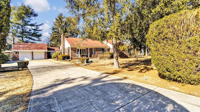 view of front of house featuring a garage, concrete driveway, stone siding, a chimney, and an outbuilding