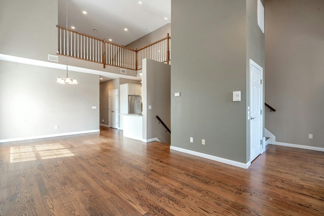 unfurnished living room featuring visible vents, an inviting chandelier, baseboards, and wood finished floors