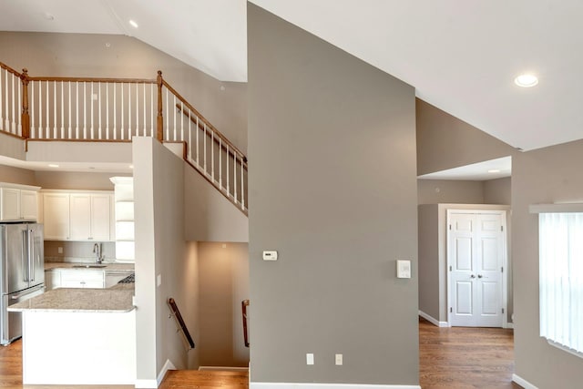 stairs with a healthy amount of sunlight, high vaulted ceiling, baseboards, and wood finished floors