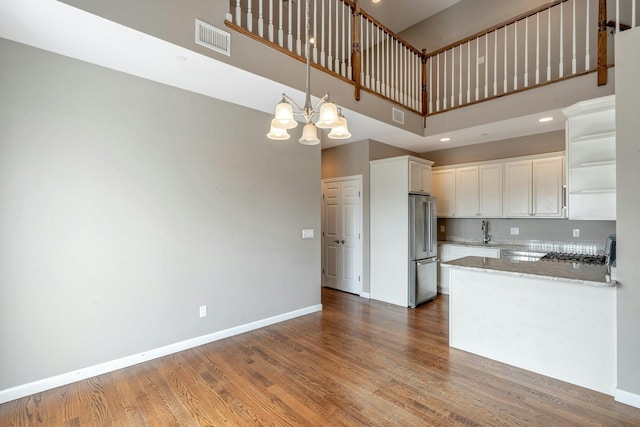 kitchen with wood finished floors, visible vents, high end fridge, white cabinetry, and a notable chandelier