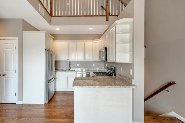 kitchen featuring open shelves, a sink, wood finished floors, stainless steel appliances, and a peninsula