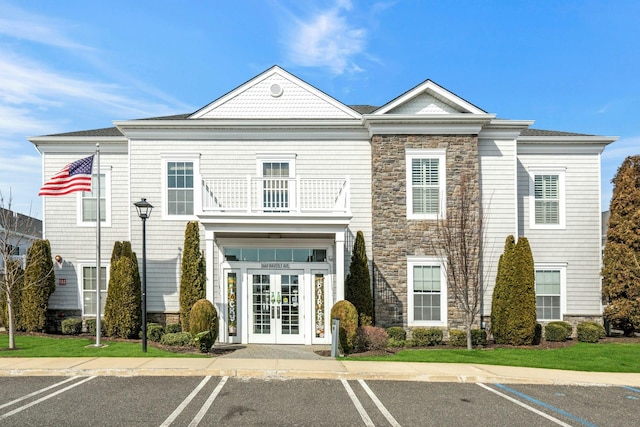 exterior space with french doors, stone siding, a balcony, and uncovered parking