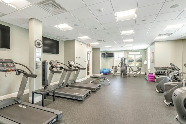 gym with a paneled ceiling, visible vents, baseboards, and a wall mounted AC