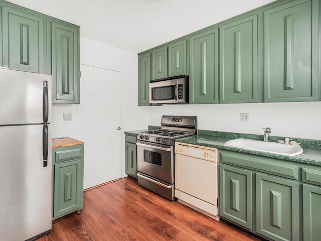 kitchen featuring dark countertops, dark wood-style flooring, a sink, stainless steel appliances, and green cabinetry