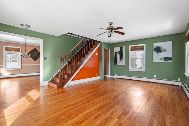 unfurnished living room featuring a baseboard heating unit, plenty of natural light, stairway, and wood finished floors