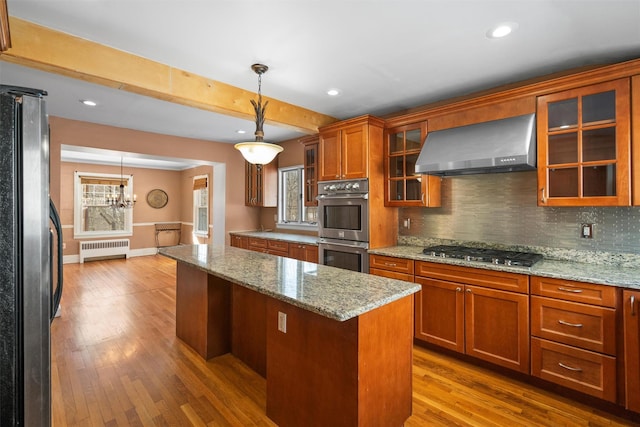 kitchen featuring radiator, wall chimney exhaust hood, glass insert cabinets, and stainless steel appliances