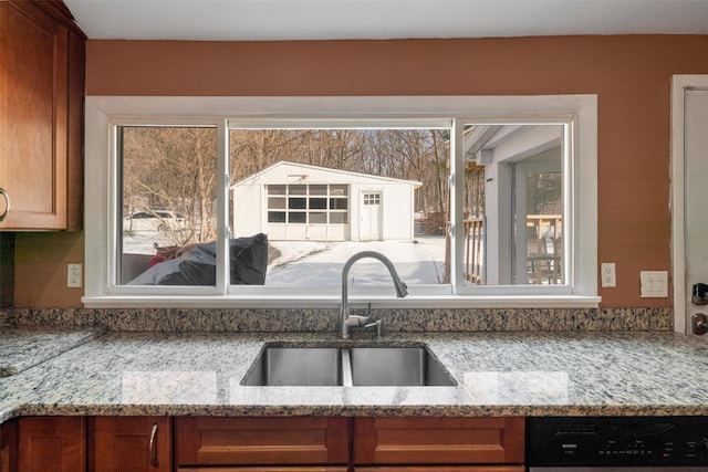 kitchen with light stone counters, brown cabinetry, a sink, and dishwasher