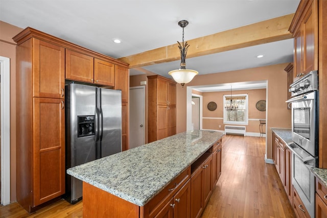 kitchen featuring radiator, appliances with stainless steel finishes, brown cabinetry, and hanging light fixtures