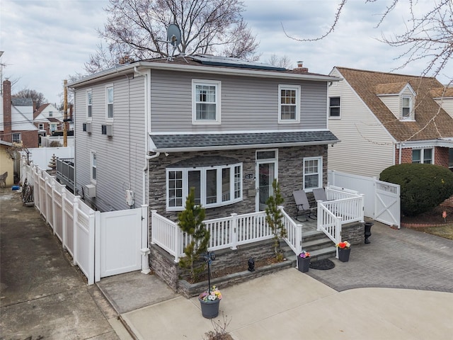 view of front of home featuring solar panels, fence private yard, a chimney, stone siding, and a gate