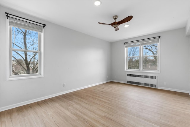 spare room with recessed lighting, light wood-style flooring, radiator heating unit, a ceiling fan, and baseboards