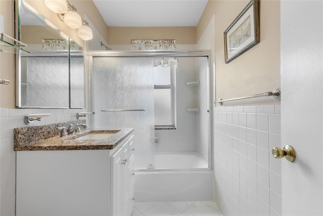 full bathroom featuring combined bath / shower with glass door, tile walls, and vanity