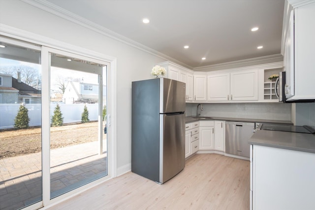 kitchen with white cabinets, dark countertops, ornamental molding, stainless steel appliances, and a sink