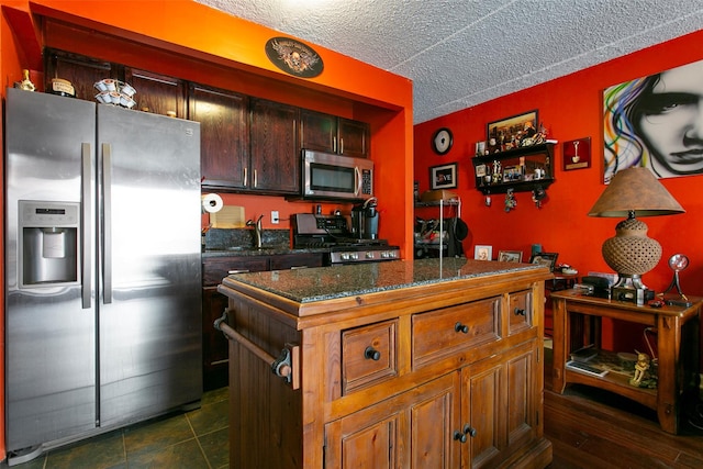 kitchen with dark stone counters, dark tile patterned flooring, a center island, stainless steel appliances, and a textured ceiling