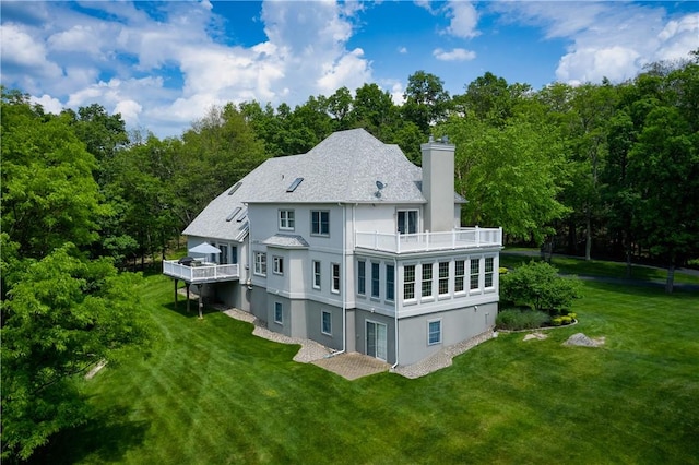 back of house with a balcony, a chimney, a yard, a wooden deck, and stucco siding