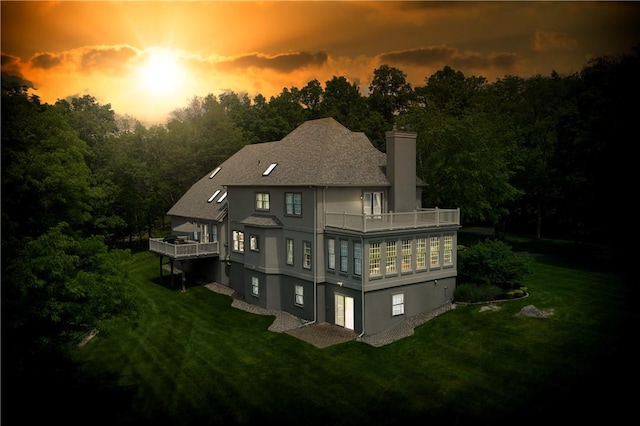 back of house with a yard, a chimney, a balcony, and stucco siding