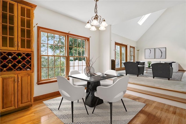 dining space with a skylight, baseboards, high vaulted ceiling, light wood-style floors, and a chandelier