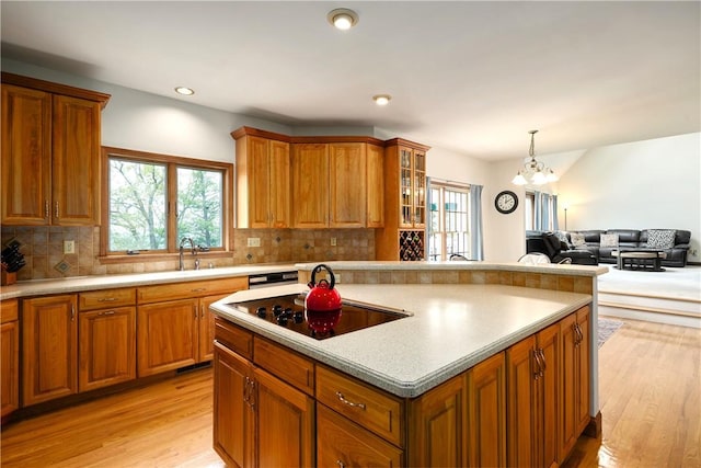 kitchen featuring brown cabinetry, glass insert cabinets, a center island, black electric stovetop, and light countertops