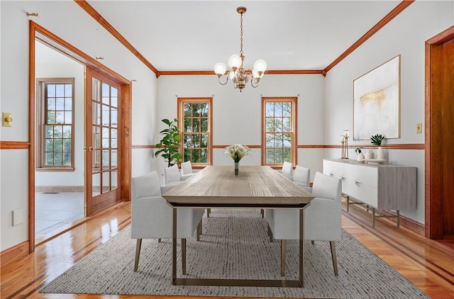 dining space featuring baseboards, ornamental molding, light wood-type flooring, and a notable chandelier