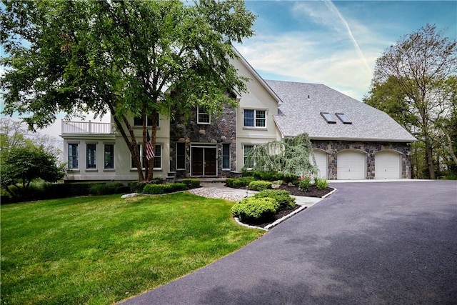 view of front of home featuring aphalt driveway, a balcony, stone siding, stucco siding, and a front yard